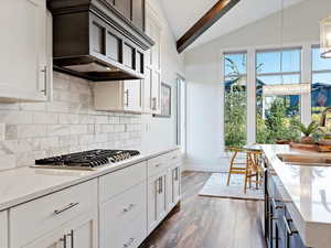 Kitchen with light stone countertops, vaulted ceiling with beams, white cabinetry, and sink