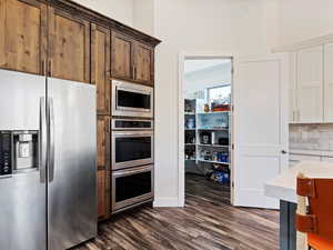 Kitchen featuring appliances with stainless steel finishes, dark hardwood / wood-style flooring, dark brown cabinetry, and backsplash