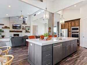 Kitchen featuring stainless steel appliances, dark hardwood / wood-style flooring, high vaulted ceiling, an island with sink, and a fireplace