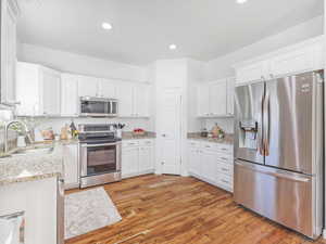 Kitchen featuring light stone countertops, appliances with stainless steel finishes, sink, white cabinets, and light hardwood / wood-style floors