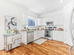 Kitchen with white cabinets, light hardwood / wood-style floors, and appliances with stainless steel finishes