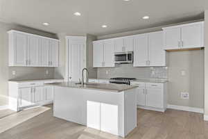 Kitchen featuring white cabinetry, appliances with stainless steel finishes, a kitchen island with sink, and sink