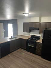 Kitchen featuring dark brown cabinets, a textured ceiling, sink, black appliances, and light hardwood / wood-style floors