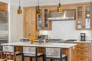 Kitchen with appliances with stainless steel finishes, decorative light fixtures, a breakfast bar area, and range hood