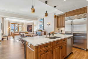 Kitchen featuring pendant lighting, a center island with sink, sink, light hardwood / wood-style flooring, and stainless steel appliances