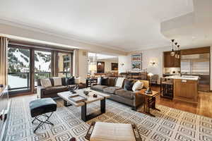 Living room with a notable chandelier, light hardwood / wood-style floors, sink, and crown molding