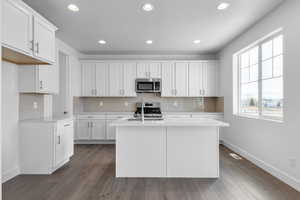 Kitchen with stainless steel appliances, dark wood-type flooring, an island with sink, and light countertops