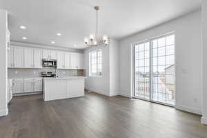 Kitchen featuring light countertops, decorative backsplash, appliances with stainless steel finishes, dark wood-style floors, and white cabinets