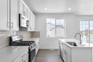 Kitchen with tasteful backsplash, dark wood finished floors, light countertops, appliances with stainless steel finishes, and a sink