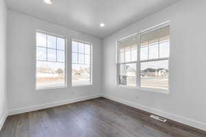 Empty room with a wealth of natural light, visible vents, baseboards, and dark wood-type flooring