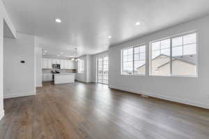 Unfurnished living room with a chandelier, a textured ceiling, baseboards, and dark wood-style flooring