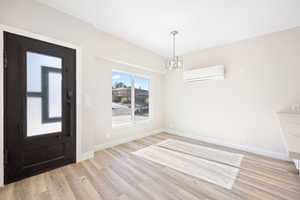 Foyer entrance with a wall mounted air conditioner, a chandelier, and light hardwood / wood-style flooring