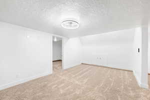 Bonus room featuring light colored carpet, lofted ceiling, and a textured ceiling