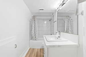 Bathroom with hardwood / wood-style floors, vanity, shower / bath combo with shower curtain, and a textured ceiling