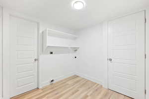 Clothes washing area featuring hookup for an electric dryer and light wood-type flooring