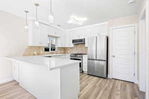 Kitchen featuring kitchen peninsula, light hardwood / wood-style flooring, white cabinets, and appliances with stainless steel finishes