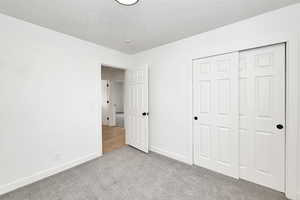 Unfurnished bedroom with light carpet, a textured ceiling, and a closet