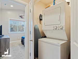 Laundry room featuring light colored carpet and stacked washer and clothes dryer