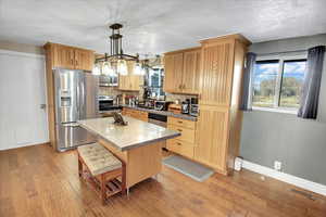 Kitchen with appliances with stainless steel finishes, tasteful backsplash, a center island, light hardwood / wood-style floors, and hanging light fixtures