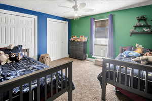 Bedroom with carpet, ceiling fan, a textured ceiling, and multiple closets