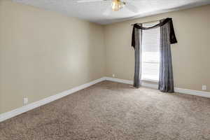 Carpeted empty room with ceiling fan and a textured ceiling