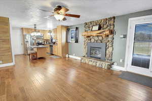 Unfurnished living room featuring a fireplace, ceiling fan, light wood-type flooring, and a textured ceiling