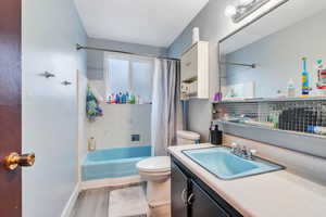 Full bathroom with wood-type flooring, vanity, toilet, and shower / bath combination with curtain