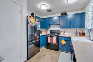 Kitchen featuring sink, black range with gas stovetop, blue cabinets, backsplash, and stainless steel fridge