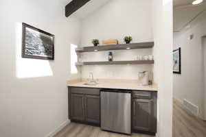 Bar with dark brown cabinetry, dishwasher, sink, vaulted ceiling with beams, and light wood-type flooring