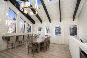 Dining space featuring beamed ceiling, high vaulted ceiling, light hardwood / wood-style floors, and wooden walls