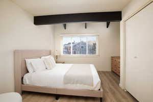 Bedroom with light hardwood / wood-style floors, beam ceiling, and a closet