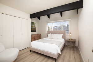 Bedroom featuring beam ceiling, light wood-type flooring, and a closet