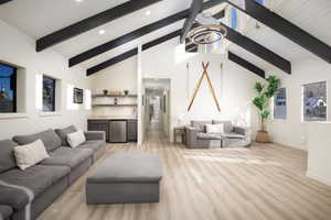 Living room featuring an inviting chandelier, high vaulted ceiling, beamed ceiling, indoor wet bar, and light hardwood / wood-style floors