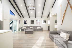 Living room featuring beamed ceiling, light hardwood / wood-style floors, a notable chandelier, and high vaulted ceiling