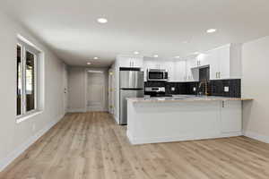 Kitchen with kitchen peninsula, backsplash, stainless steel appliances, light hardwood / wood-style flooring, and white cabinets