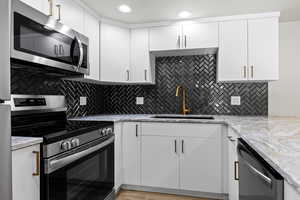 Kitchen featuring decorative backsplash, appliances with stainless steel finishes, light stone countertops, sink, and white cabinetry