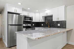 Kitchen featuring white cabinetry, light stone counters, kitchen peninsula, appliances with stainless steel finishes, and light wood-type flooring