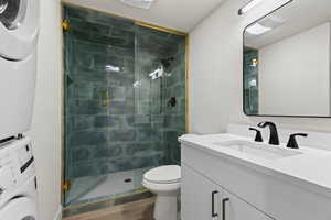 Bathroom featuring vanity, hardwood / wood-style flooring, toilet, stacked washing maching and dryer, and a shower with shower door