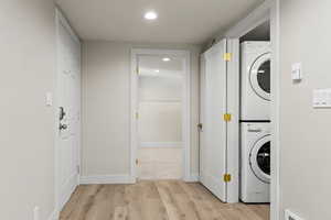 Clothes washing area featuring light wood-type flooring and stacked washer and clothes dryer