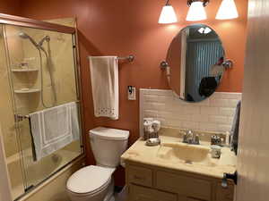 Full bathroom with decorative backsplash, vanity, toilet, and bath / shower combo with glass door