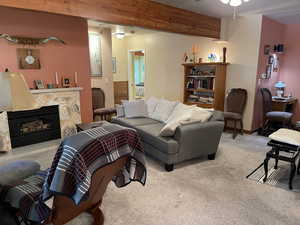 Carpeted living room featuring a stone fireplace and ceiling fan