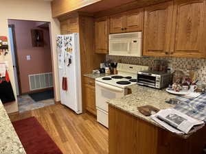 Kitchen featuring decorative backsplash, light hardwood / wood-style floors, light stone countertops, and white appliances