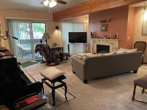 Carpeted living room featuring ceiling fan and beam ceiling