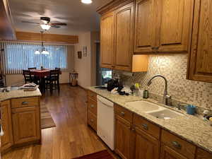 Kitchen featuring pendant lighting, dishwasher, ceiling fan with notable chandelier, sink, and dark hardwood / wood-style floors