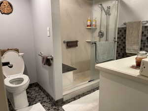 Bathroom with tile patterned floors, vanity, toilet, and a shower with door