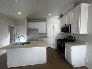 Kitchen with white cabinetry, sink, dark hardwood / wood-style flooring, an island with sink, and appliances with stainless steel finishes