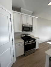 Kitchen with white cabinets, light hardwood / wood-style floors, and appliances with stainless steel finishes