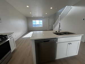 Kitchen with sink, light wood-type flooring, an island with sink, appliances with stainless steel finishes, and white cabinetry