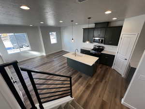 Kitchen featuring appliances with stainless steel finishes, dark hardwood / wood-style flooring, a kitchen island with sink, sink, and decorative light fixtures