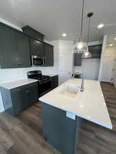 Kitchen featuring a kitchen island with sink, dark wood-type flooring, hanging light fixtures, sink, and appliances with stainless steel finishes